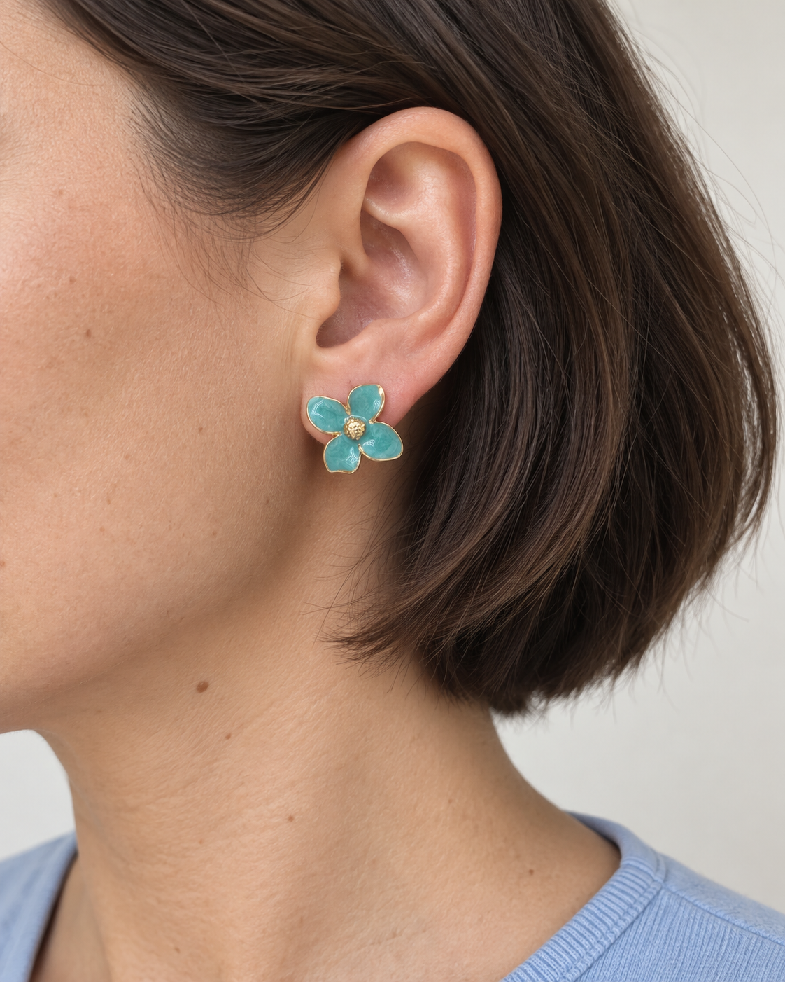 Felicia – blomformade örhängen med turkosa kronblad och guldfärgade kanter, burna på modell. ISOLDE ACCESSORIES.