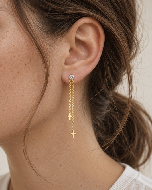 Amanda – guldfärgade örhängen med tunna kedjehängen och små korsdetaljer, burna på modell. ISOLDE ACCESSORIES.